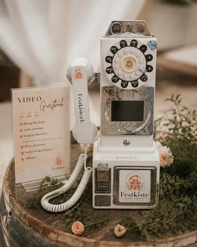 Das Video-Telefon: weisses Münztelefon im Stil der Fünfzigerjahre, mit Bildschirm, Kamera und Festkiste-Aufkleber, daneben die Anleitung für die Gäste
